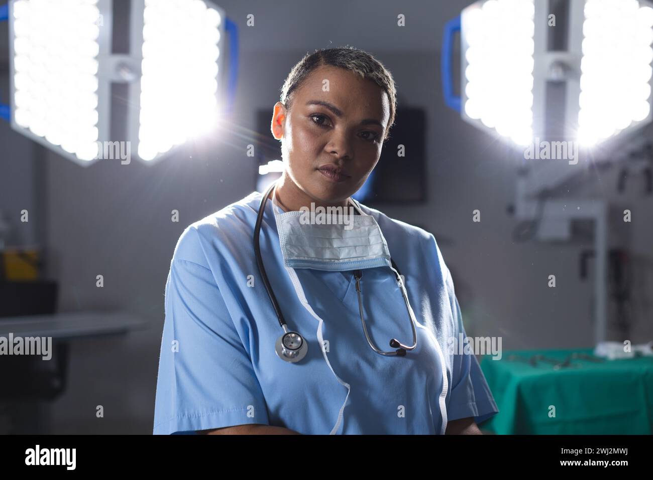 Retrato de cirujano femenino biracial usando exfoliantes y estetoscopio en quirófano Foto de stock
