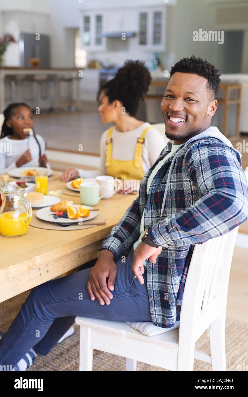 Hombre afroamericano feliz sentado en la mesa, tomando un bocadillo con la familia en casa, espacio de copia Foto de stock