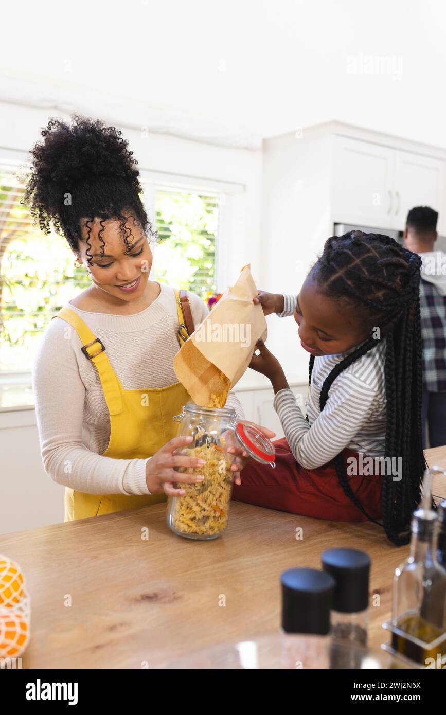 Feliz madre e hija afroamericana vertiendo pasta en frasco de vidrio en la cocina en casa, espacio de copia Foto de stock