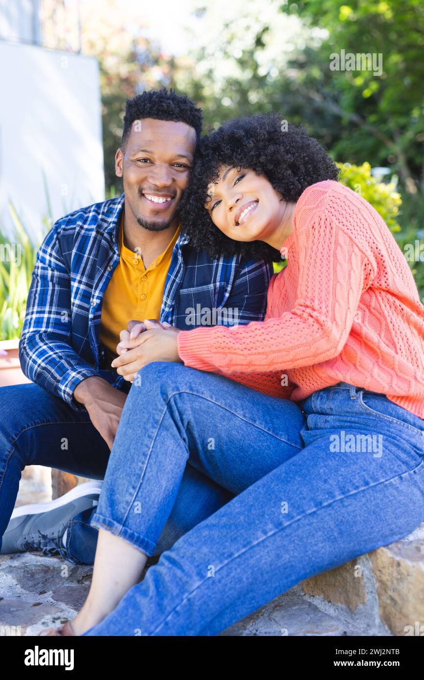 Feliz pareja afroamericana abrazando y sosteniendo de la mano en las escaleras en el jardín soleado, espacio de copia Foto de stock