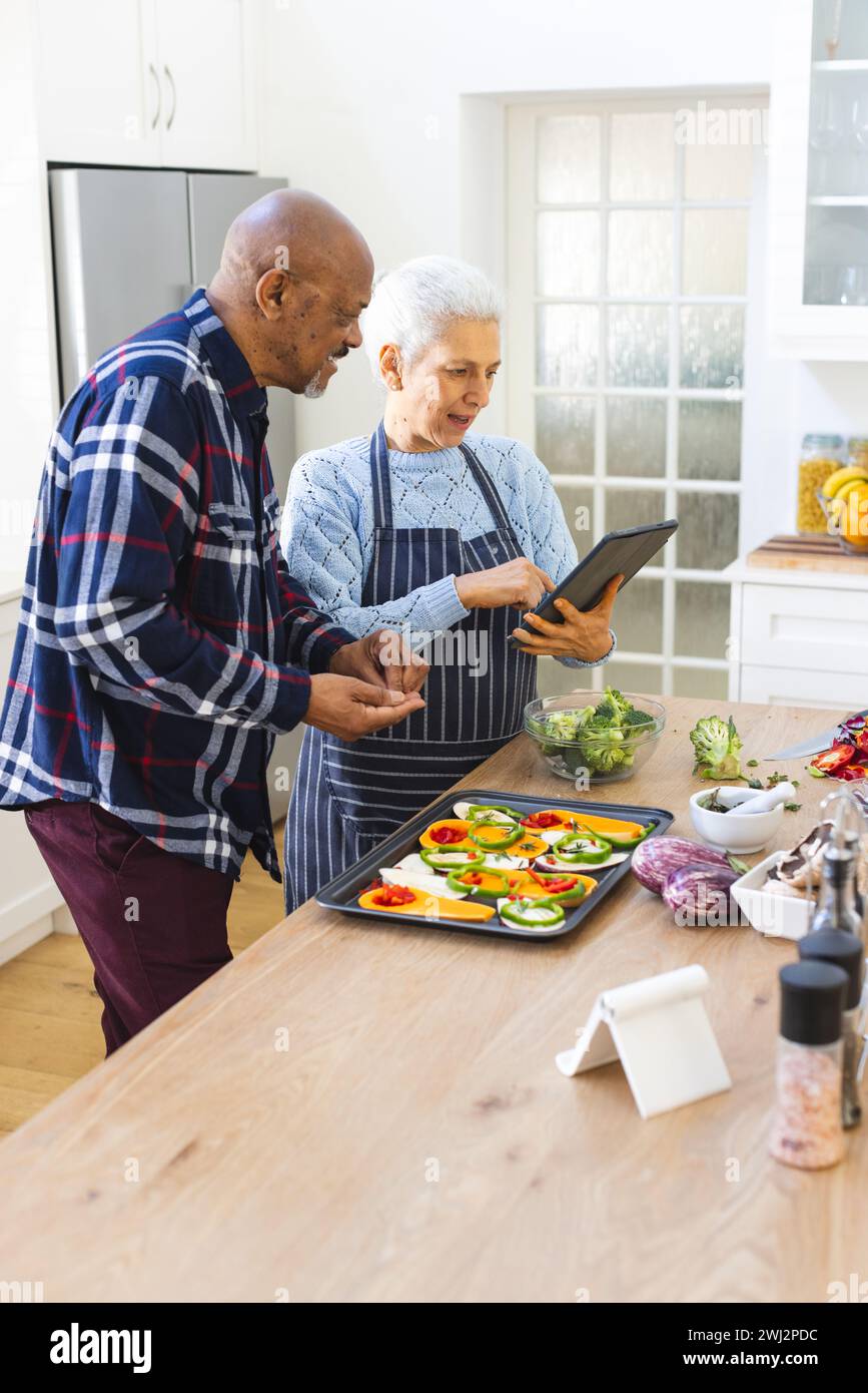 Diversa pareja mayor que prepara la comida usando tableta en la cocina Foto de stock