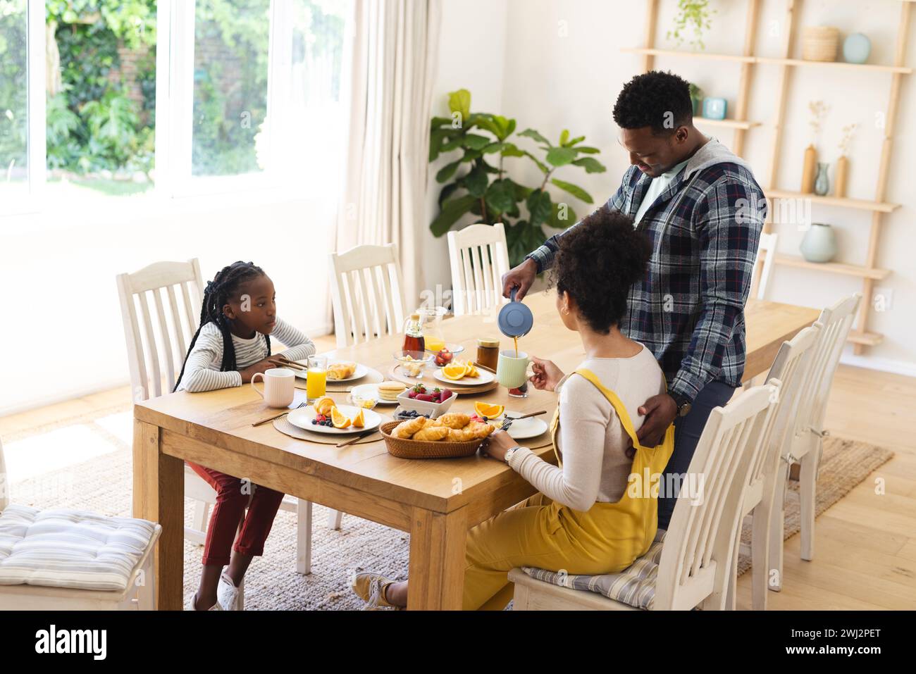 Hombre afroamericano feliz vertiendo té a taza en el desayuno en la mañana en casa, copiar espacio Foto de stock
