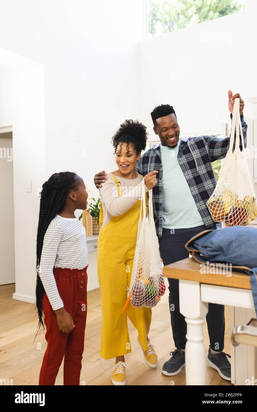 Familia afroamericana feliz poniendo comestibles en la mesa en la cocina en casa, espacio de copia Foto de stock