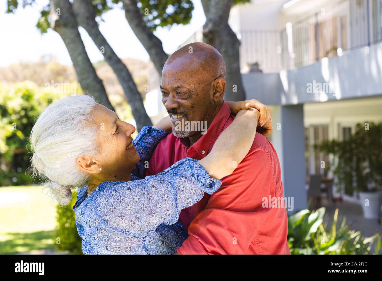 Feliz pareja senior diversa abrazando en jardín soleado Foto de stock