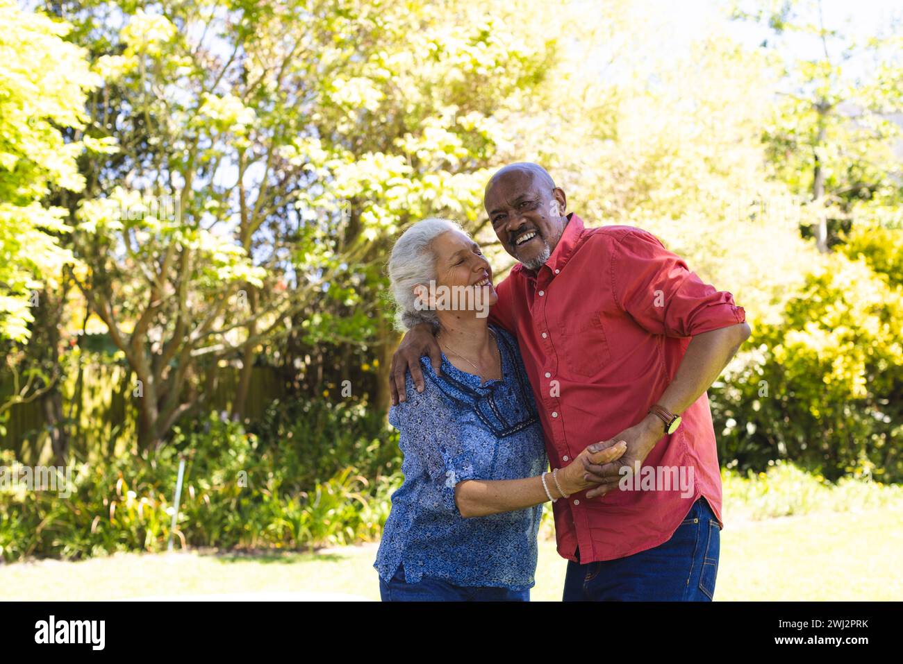 Feliz pareja senior diversa bailando en jardín soleado Foto de stock