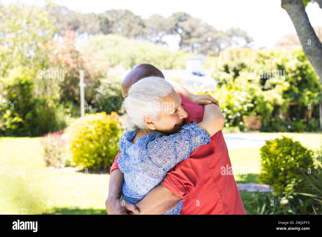 Feliz pareja senior diversa abrazándose en el jardín soleado Foto de stock