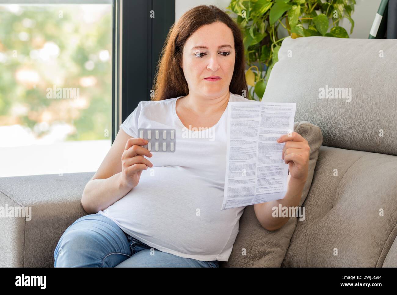 Foto de una mujer embarazada confundida leyendo un folleto antes de tomar una pastilla en casa Foto de stock