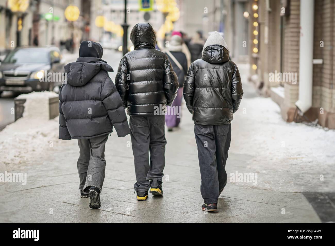 Vista trasera de los hombres jóvenes caminando en el entorno urbano en invierno. La vida moderna de la ciudad. Fotografía callejera cándida Foto de stock