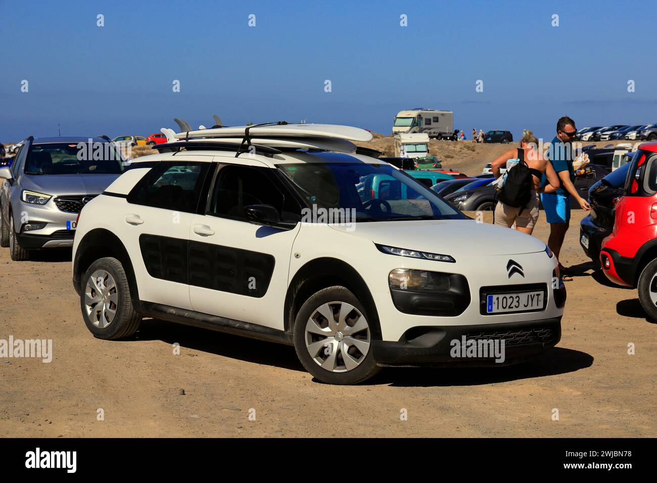 Coche blanco con tablas de surf en el portaequipajes en un aparcamiento de la playa haciendo cola para salir. Playa de La Conca, Fuerteventura tomada en noviembre de 2023 Foto de stock