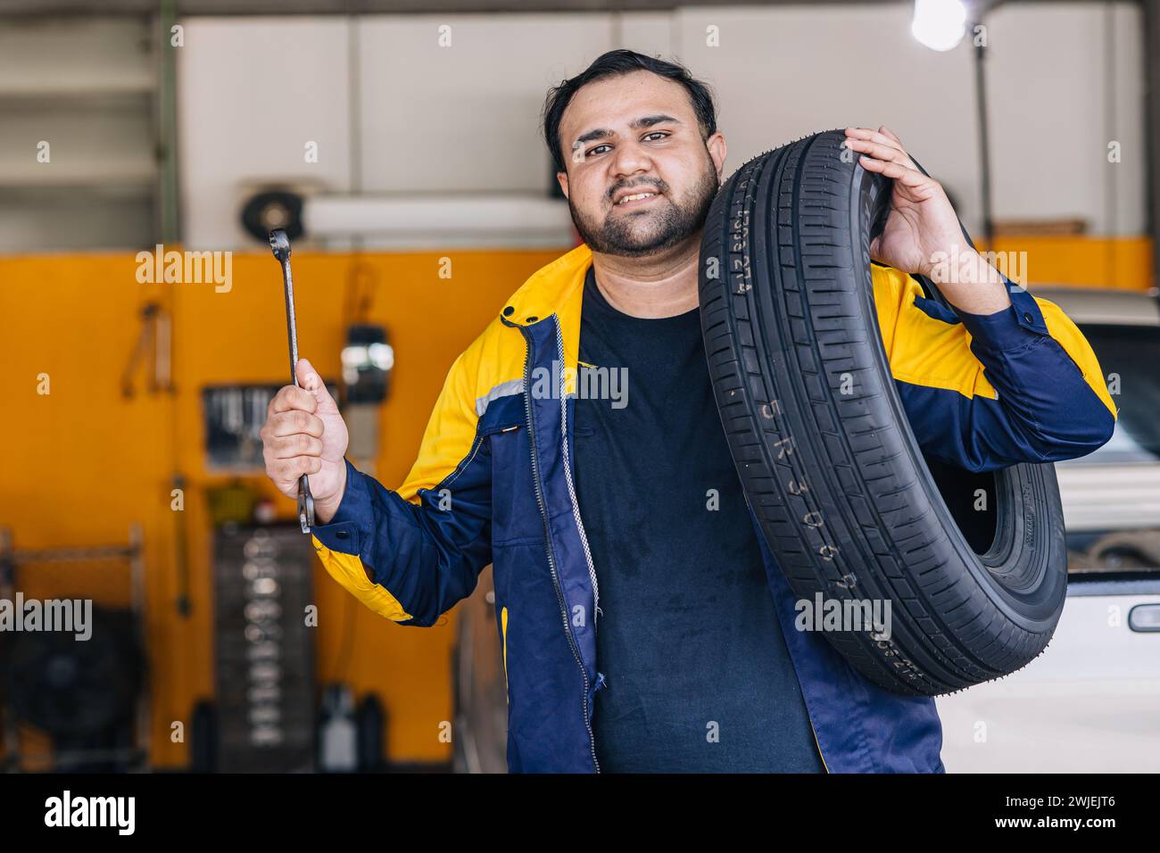 Trabajador indio del hombre del retrato en el servicio del coche del trabajo feliz del mecánico auto del garaje substituye el mantenimiento del vehículo del neumático Foto de stock