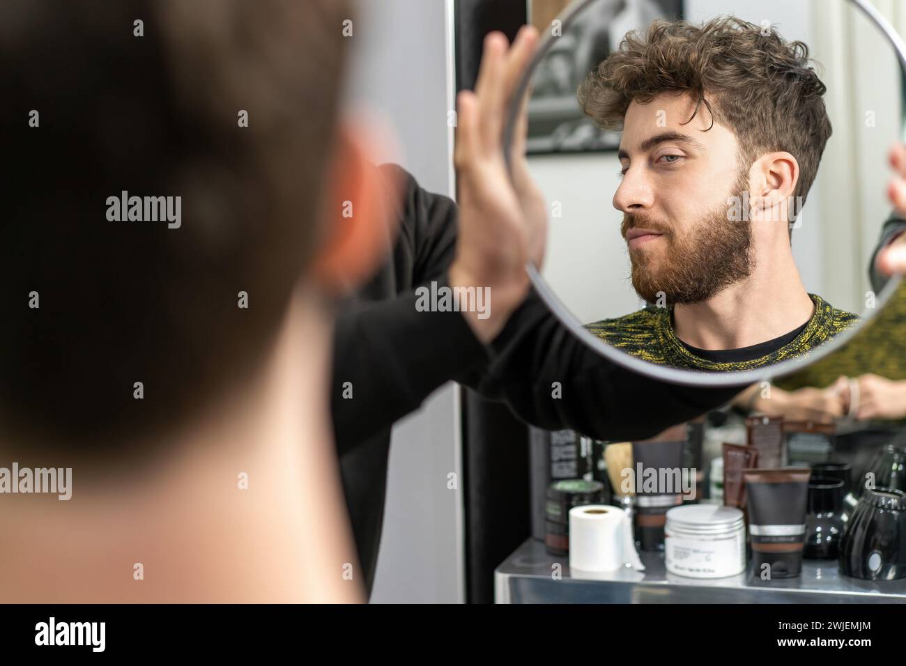 Hombre joven ajustando su peinado en el espejo - se centró en el aseo personal y el estilo. Foto de stock