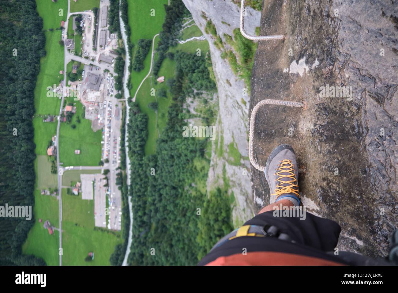 Pasos turísticos en metal a través de soportes de ferrata, en el borde de una pared de roca, con una enorme brecha vertical debajo de él y una vista del valle de abajo. Acción de verano Foto de stock