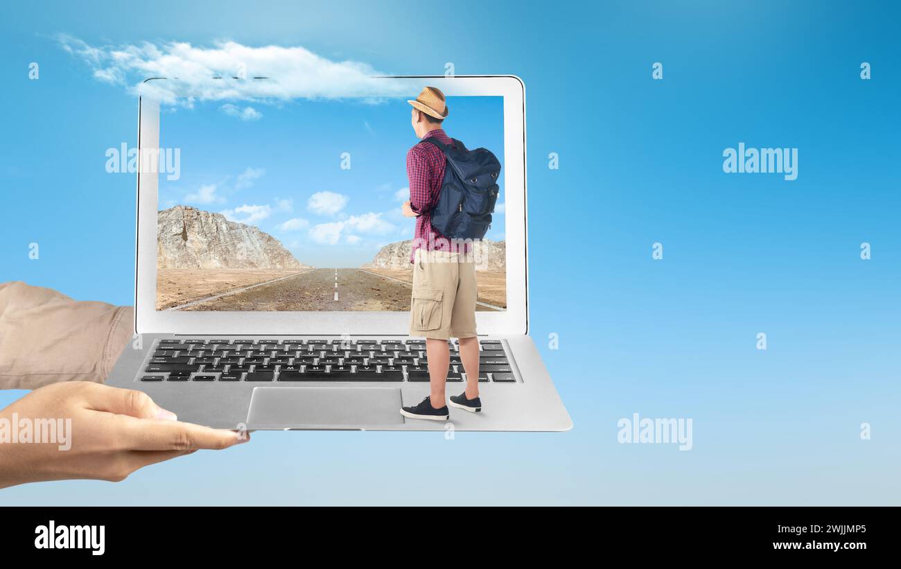 Una mano humana sosteniendo una computadora portátil con un hombre asiático en un sombrero y una mochila de pie con una vista de acantilado de roca y cielo azul en la pantalla del ordenador portátil. Viaje c Foto de stock