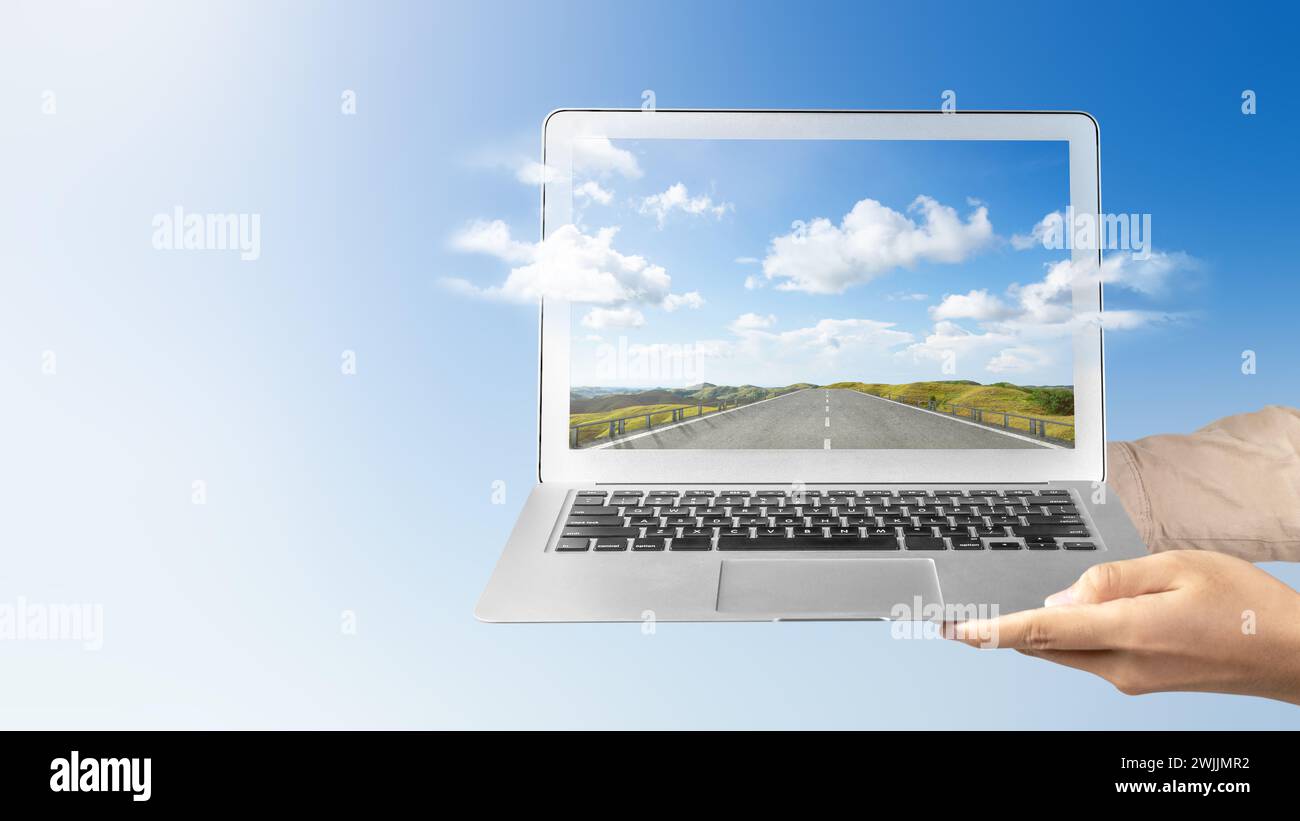 Una mano humana sosteniendo un ordenador portátil con una vista de pantalla de la calle con colinas verdes y una vista del paisaje con el cielo azul. Concepto de viaje Foto de stock