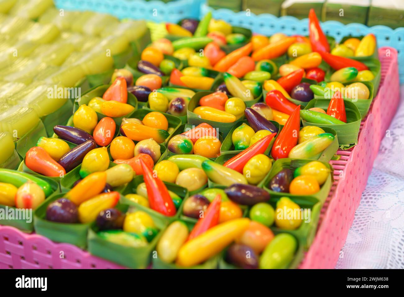 Un surtido de frutas en forma de frijoles Mung postres tailandeses vibrantes, diseñados para parecerse a frutas y verduras en miniatura, se muestran en recipientes transparentes en Foto de stock