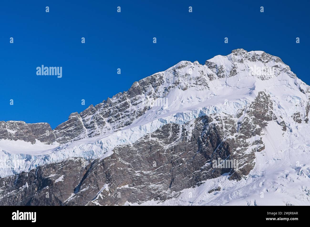 Primer plano de la montaña Icy: Impresionantes picos cubiertos de nieve contra un vibrante cielo azul Foto de stock