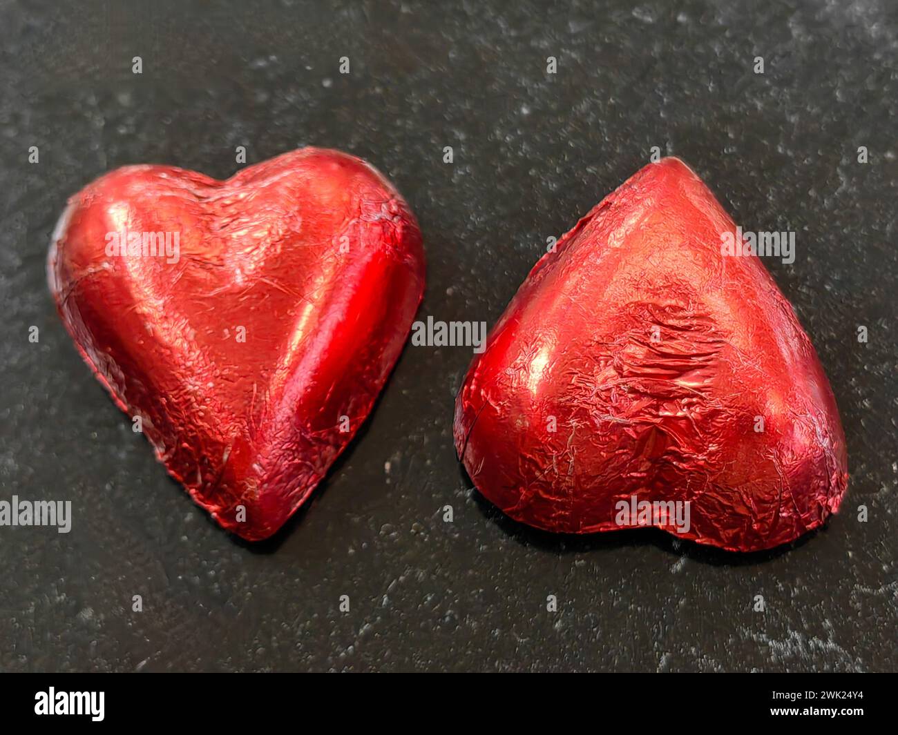 Dicotomía de caramelo. Reflexiones de género. Dos dulces de choco envueltos en forma de corazón sobre mesa negra, simbolizando al hombre y a la mujer. Feliz día de San Valentín. Foto de stock