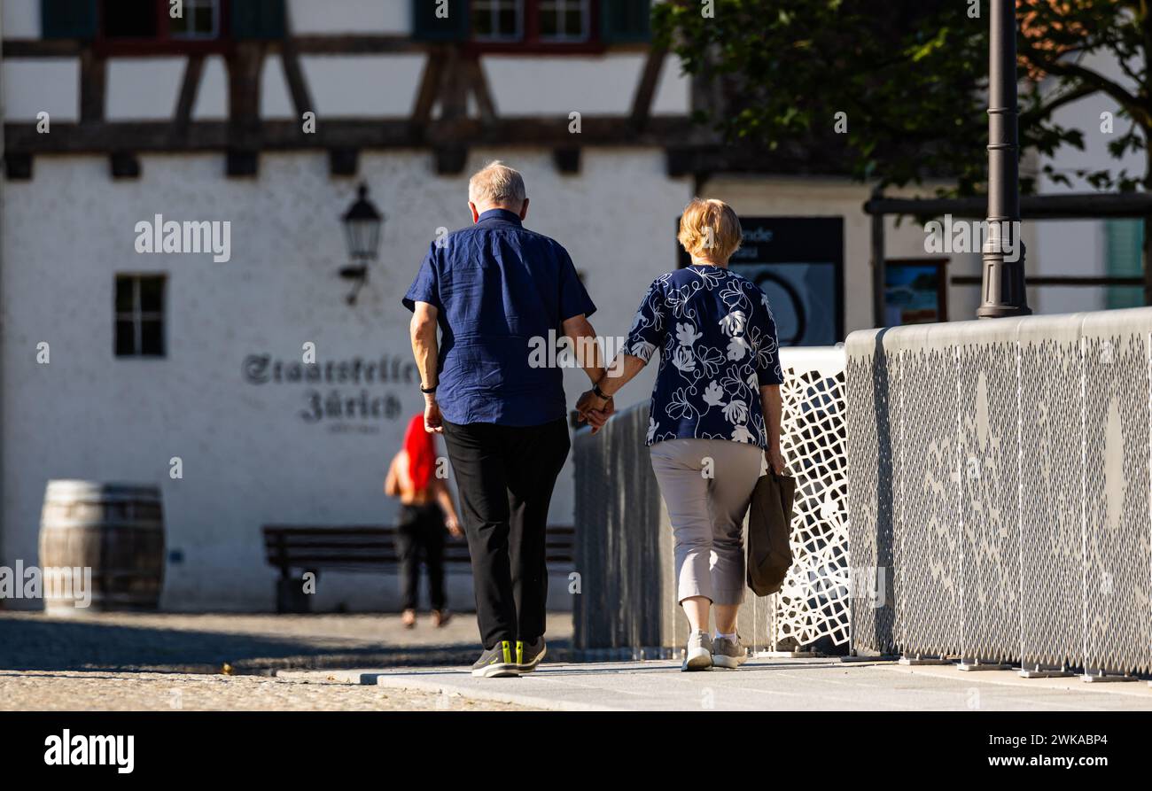 Zwei Rentner halten sich die hand und laufen über eine Brücke. (Rheinau, Schweiz, 25.06.2023) Foto de stock