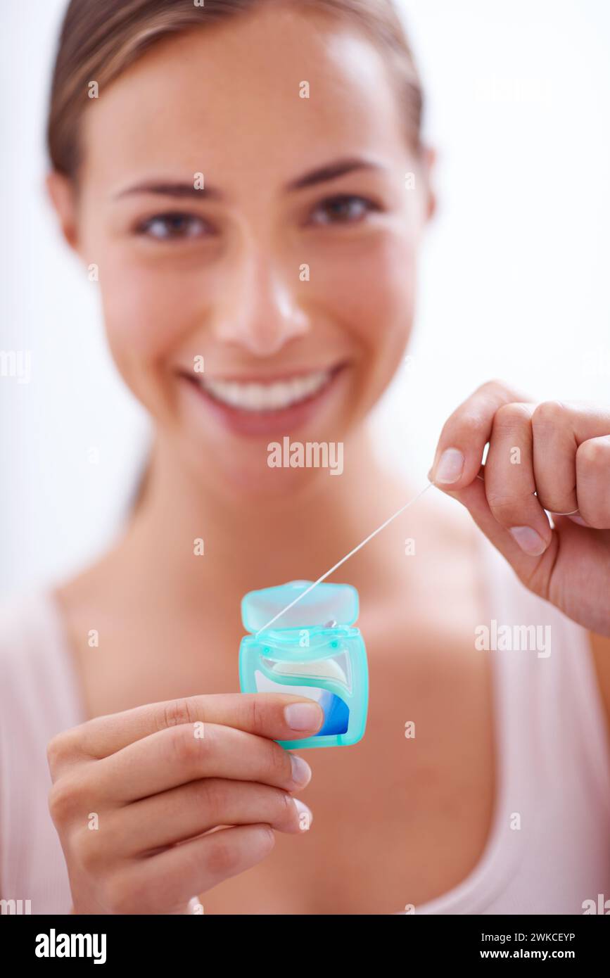 Retrato, sonrisa y hilo dental para el cuidado de la higiene oral con la  mujer en el baño de casa para el blanqueamiento de los dientes. Cara,  producto y persona joven feliz