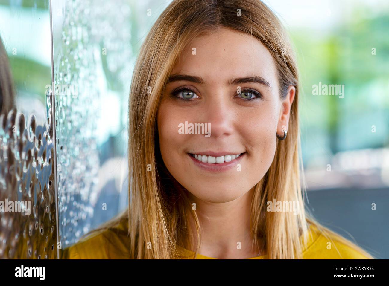 Esta imagen de primer plano muestra la cautivadora mirada de una joven con una cálida sonrisa, con un top amarillo que destaca su alegre expresión. El ba Foto de stock