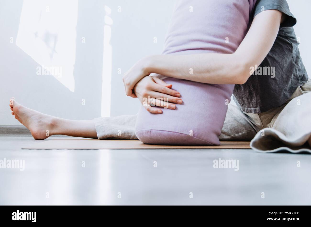 Mujer en ropa casual practicando la postura de mariposa yin yoga apoyándose en el refuerzo Foto de stock