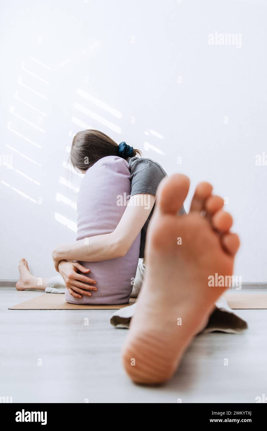 Mujer en ropa casual practicando yin yoga pierna ancha hacia adelante pose de pliegue apoyada en el refuerzo Foto de stock