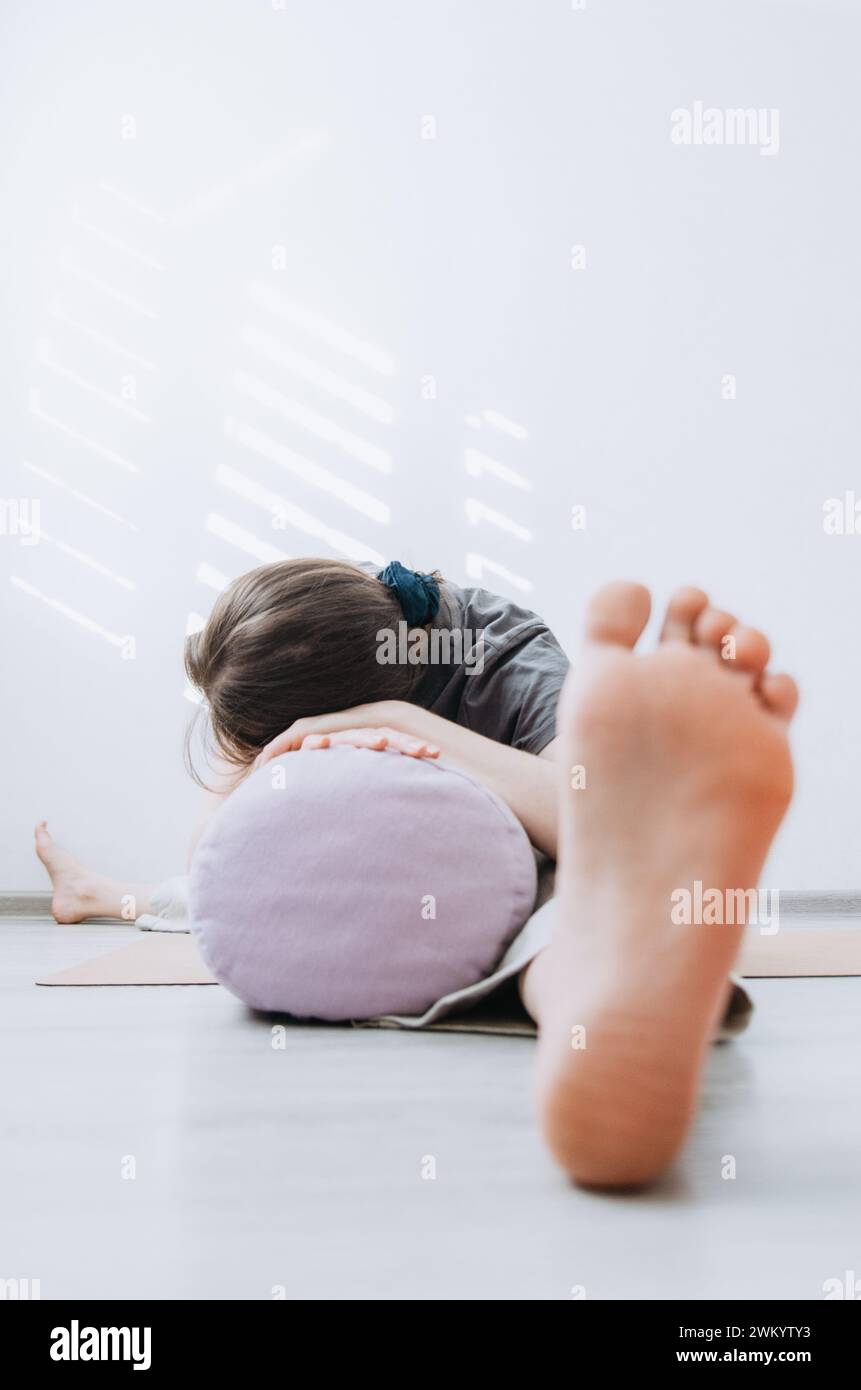 Mujer en ropa casual practicando yin yoga pierna ancha hacia adelante pliegue pose con refuerzo Foto de stock