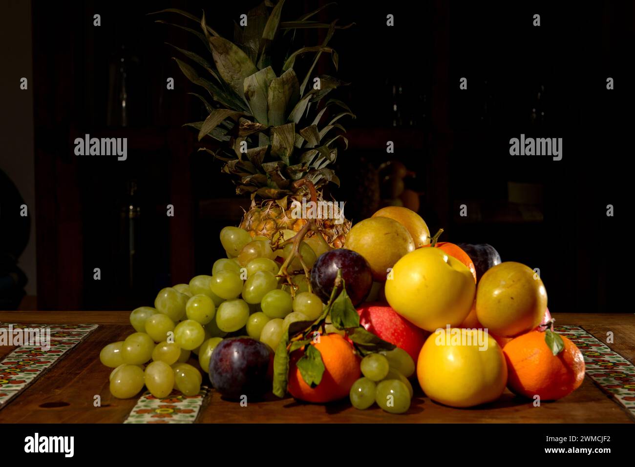 Primer plano de una pila de uvas, manzanas, satsumas, ciruelas y una piña en una mesa Foto de stock