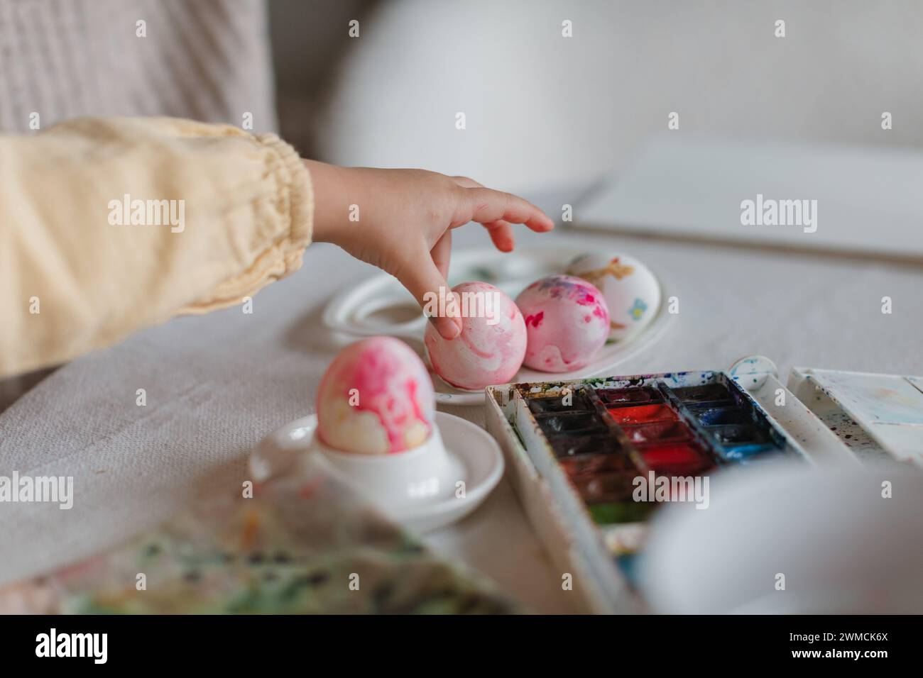 Primer plano de un niño pequeño sentado en una mesa de comedor que decora un huevo de Pascua Foto de stock