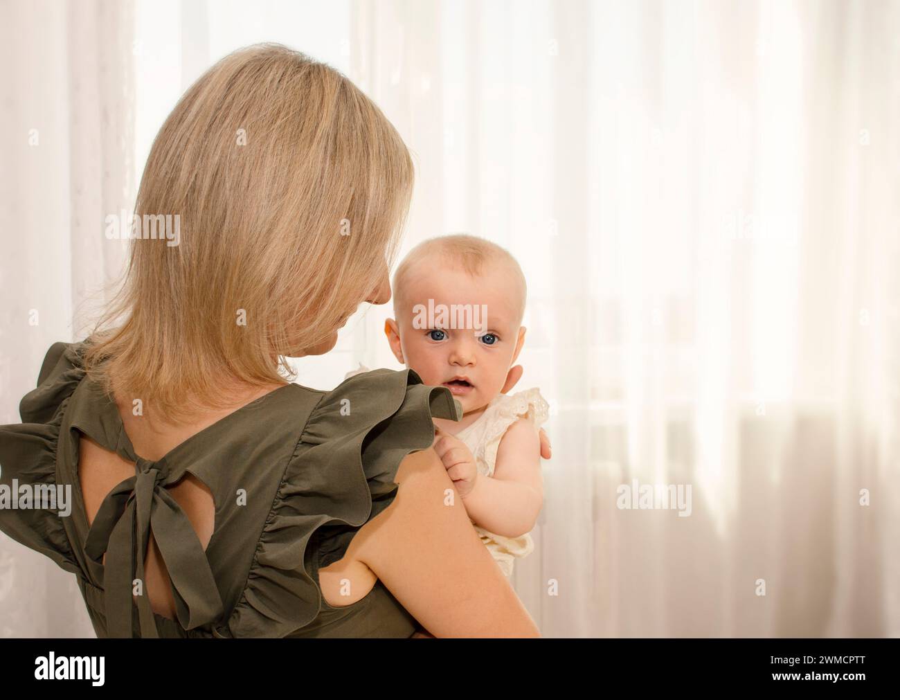 madre joven que sostiene a su bebé en sus brazos, en un día soleado en casa, espacio libre para el texto Foto de stock