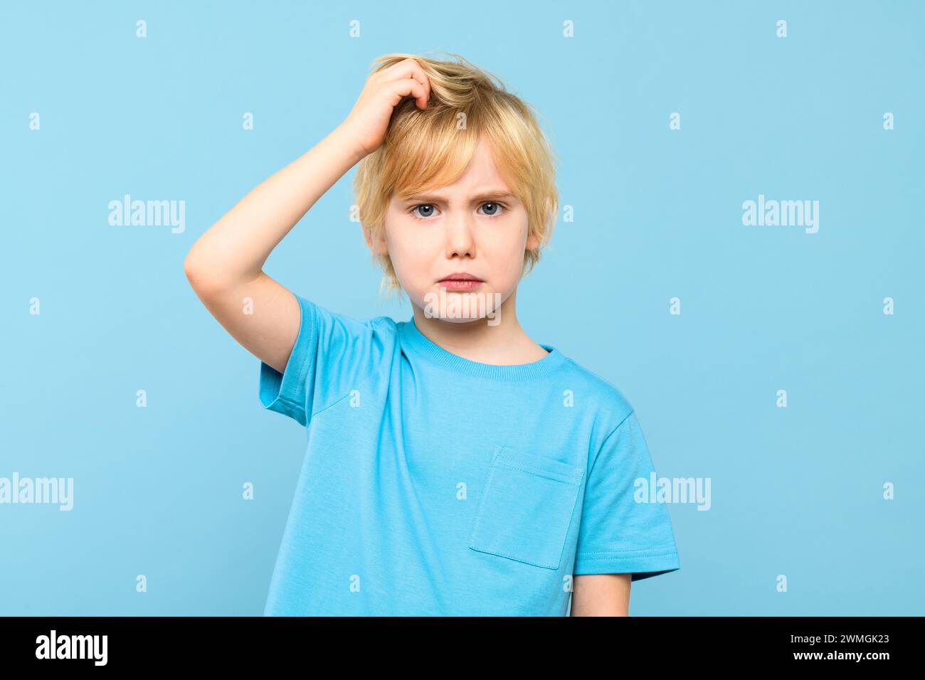 Joven dudoso niño confundido pensando, rascándose la cabeza, tratando de encontrar solución, aislado en fondo azul pastel. Foto de stock