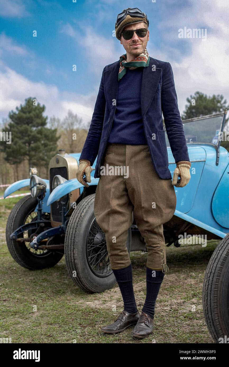 Joven posando con gorra plana y googles y atuendo de carreras en la carrera de automóviles vintage en Montlhery Revival, Linas, Francia. Foto de stock