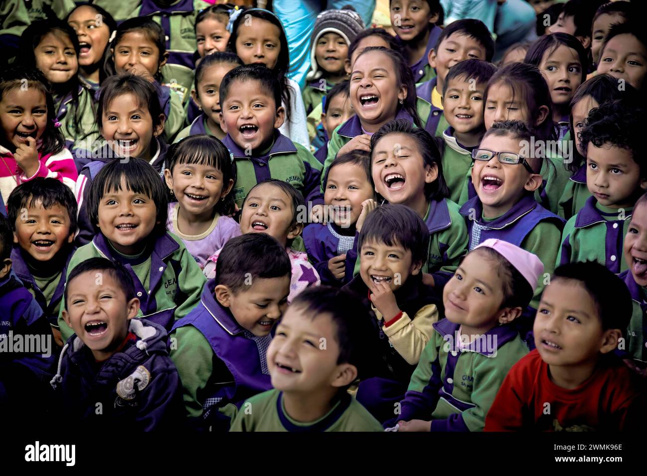 Los hijos de los trabajadores del mercado en una guardería de Quito se echaron a reír con caras alegres mientras veían a un mago, un payaso y bailarines étnicos. Foto de stock