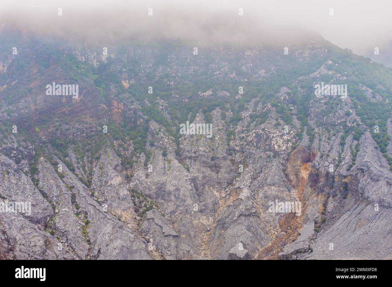 Paisaje árido con montañas brumosas, vegetación escasa y formaciones rocosas, en Indonesia Foto de stock