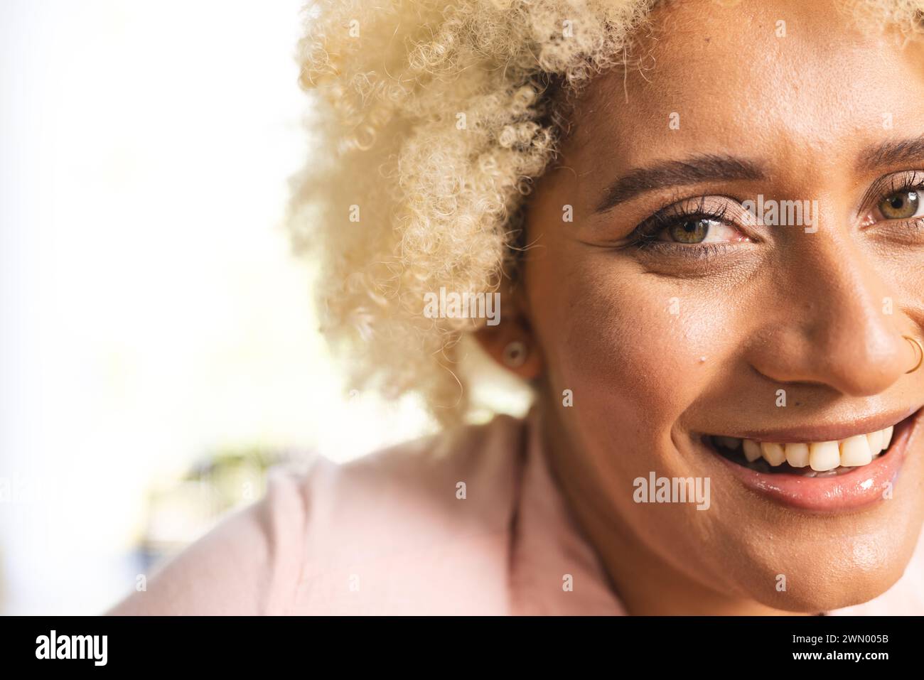 Primer plano de una joven mujer biracial con el pelo rubio rizado y una sonrisa cálida Foto de stock