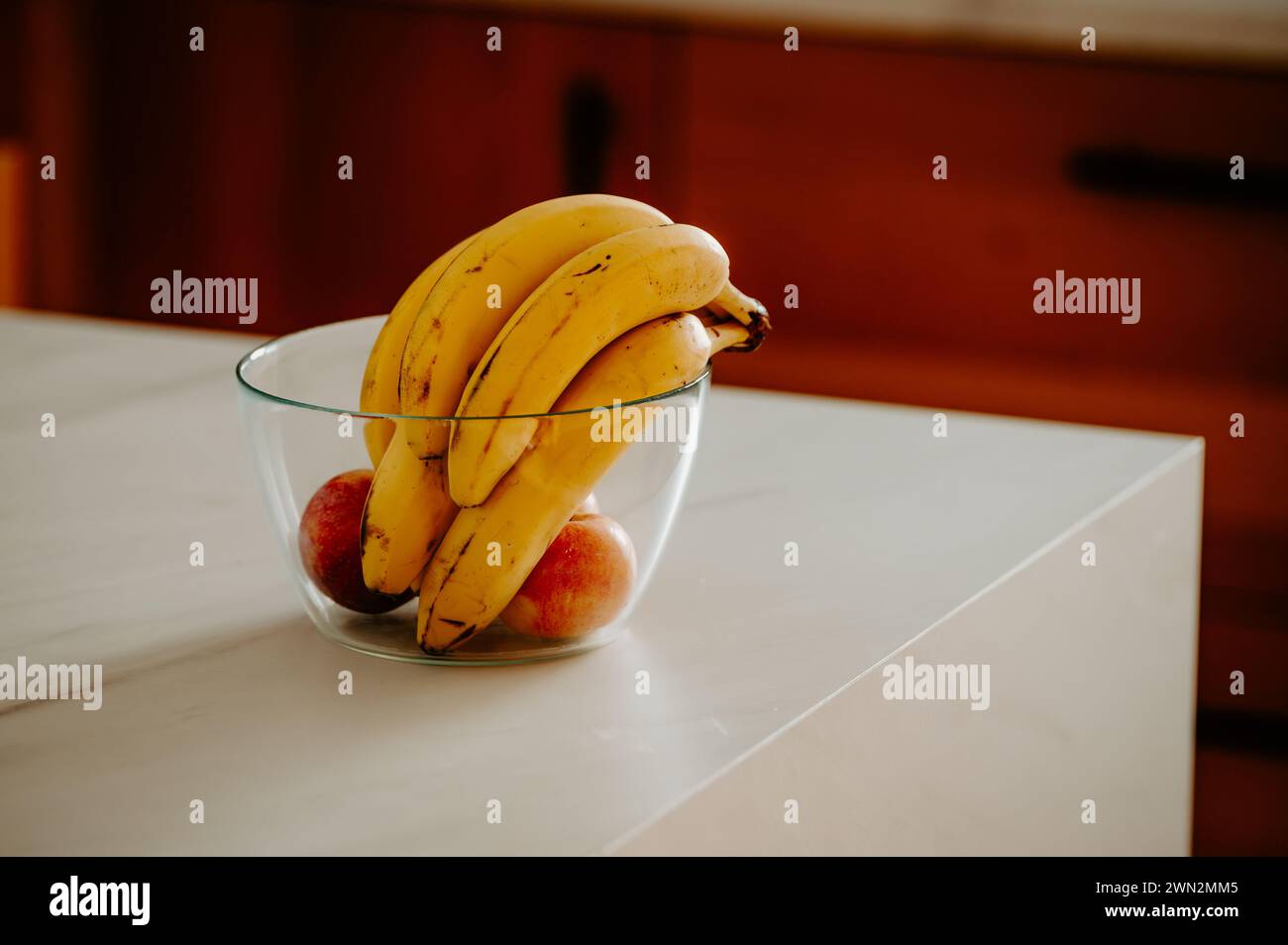 La luz del día resalta un plátano en un tazón de vidrio en el mostrador de la cocina Foto de stock