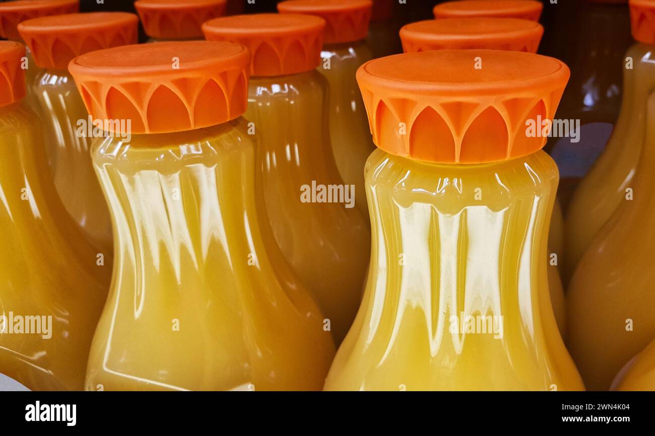 Botellas de jugo de naranja en un estante de supermercado con enfoque en primer plano. Imagen de cierre, contenedores parciales y tapas mostradas. Foto de stock