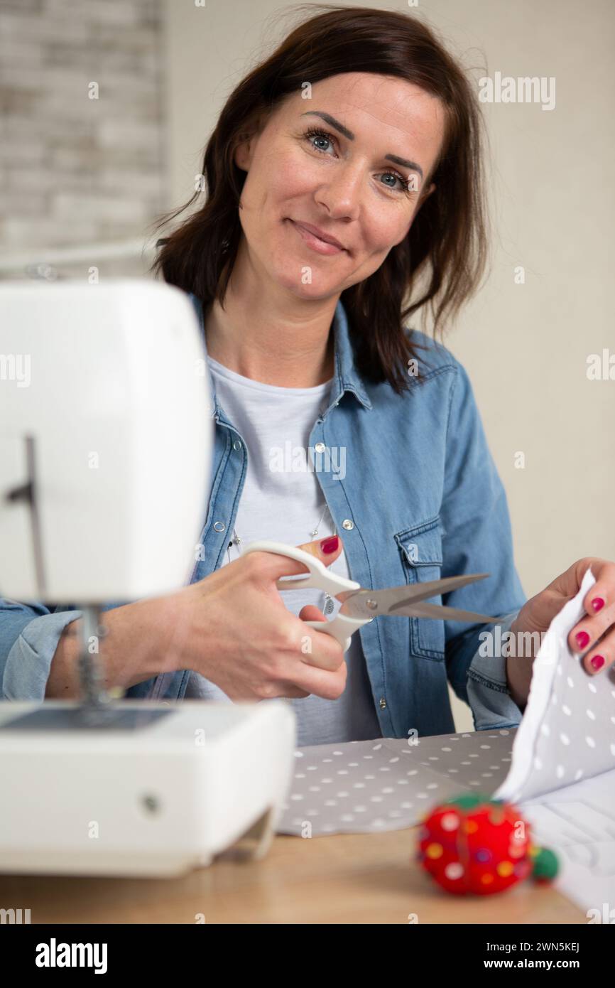 sastre femenino de mediana edad sonriente usando máquina de coser Foto de stock