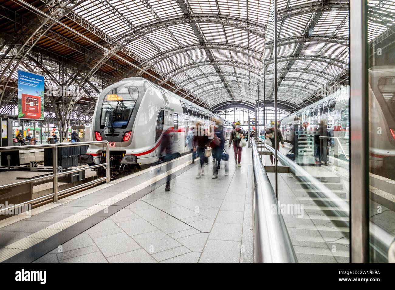 Los viajeros que esperan los trenes en una estación de vestíbulo con un techo impresionante, la estación central de Leipzig Foto de stock