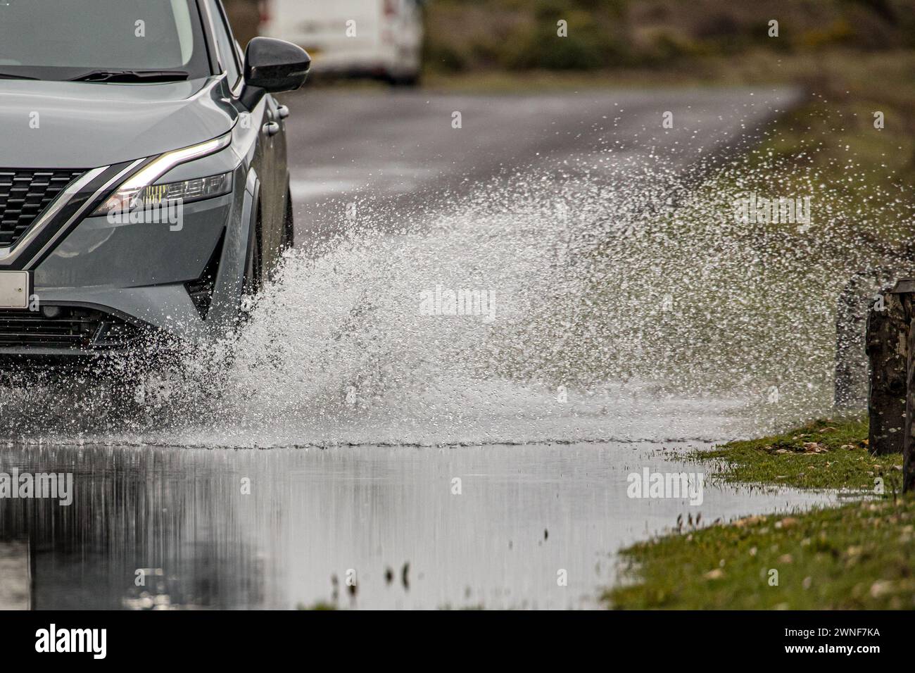 Rocío de agua de una rueda de automóvil y la sección delantera del automóvil mientras conduce a través de una carretera inundada Foto de stock