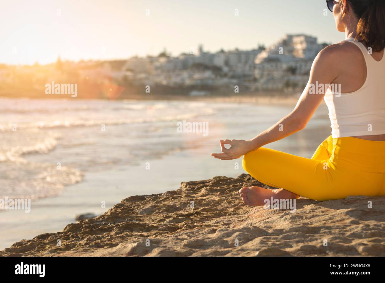 Mujer sentada meditando y practicando yoga junto al mar en el sol Foto de stock