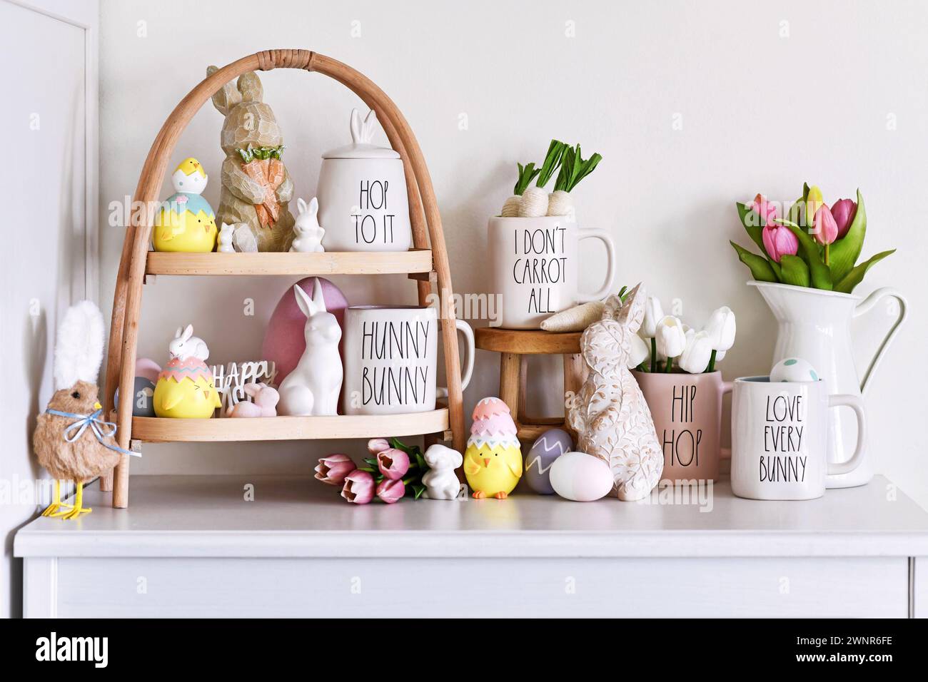 Alemania - Marzo 2024: Decoración de temporada del hogar de Pascua con bandeja, tazas de diseño Rae Dunn con texto huevo de Pascua, esculturas de conejo y tulipán primavera f Foto de stock