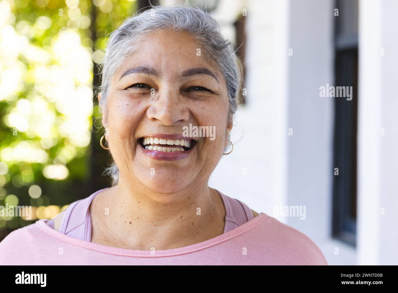 Mujer biracial mayor con el pelo gris y una sonrisa cálida, con un top rosa Foto de stock