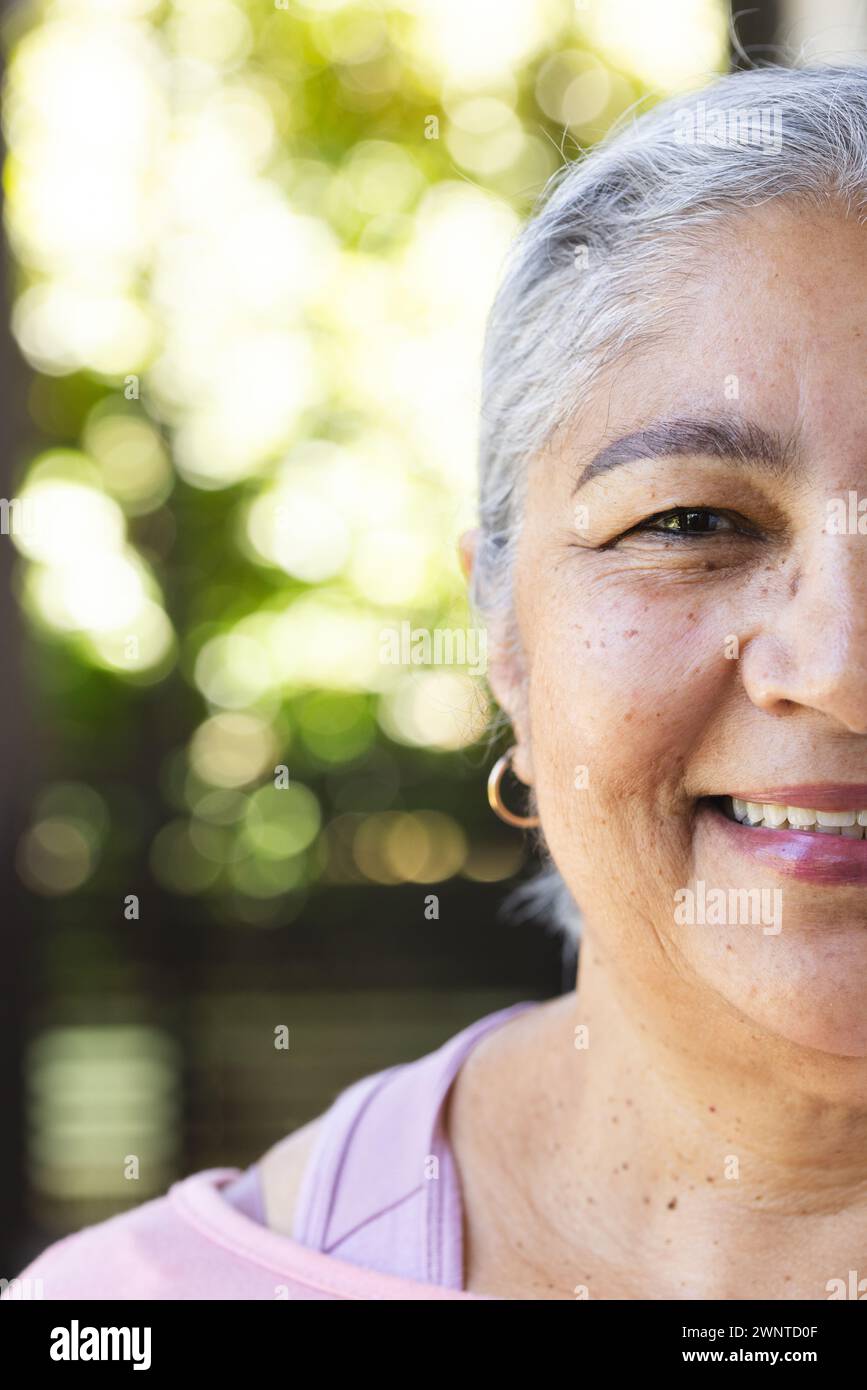 Mujer biracial mayor con el pelo gris y una sonrisa cálida se encuentra al aire libre con espacio de copia Foto de stock