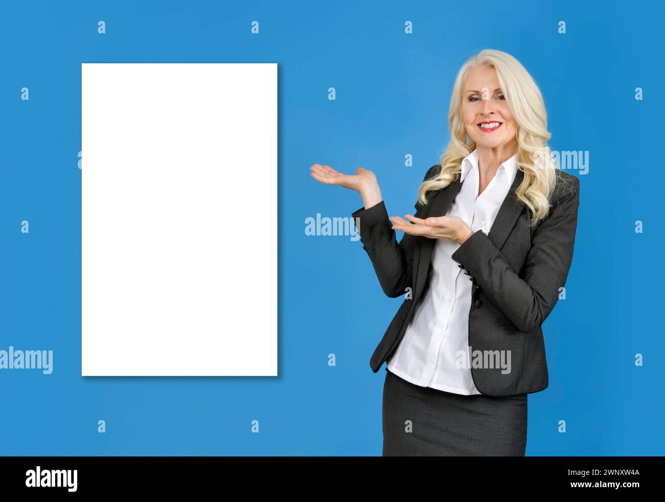 Mujer de negocios atractiva contra fondo azul con las manos apuntando hacia el espacio blanco en blanco detrás de ella. Rellene el espacio en blanco Foto de stock