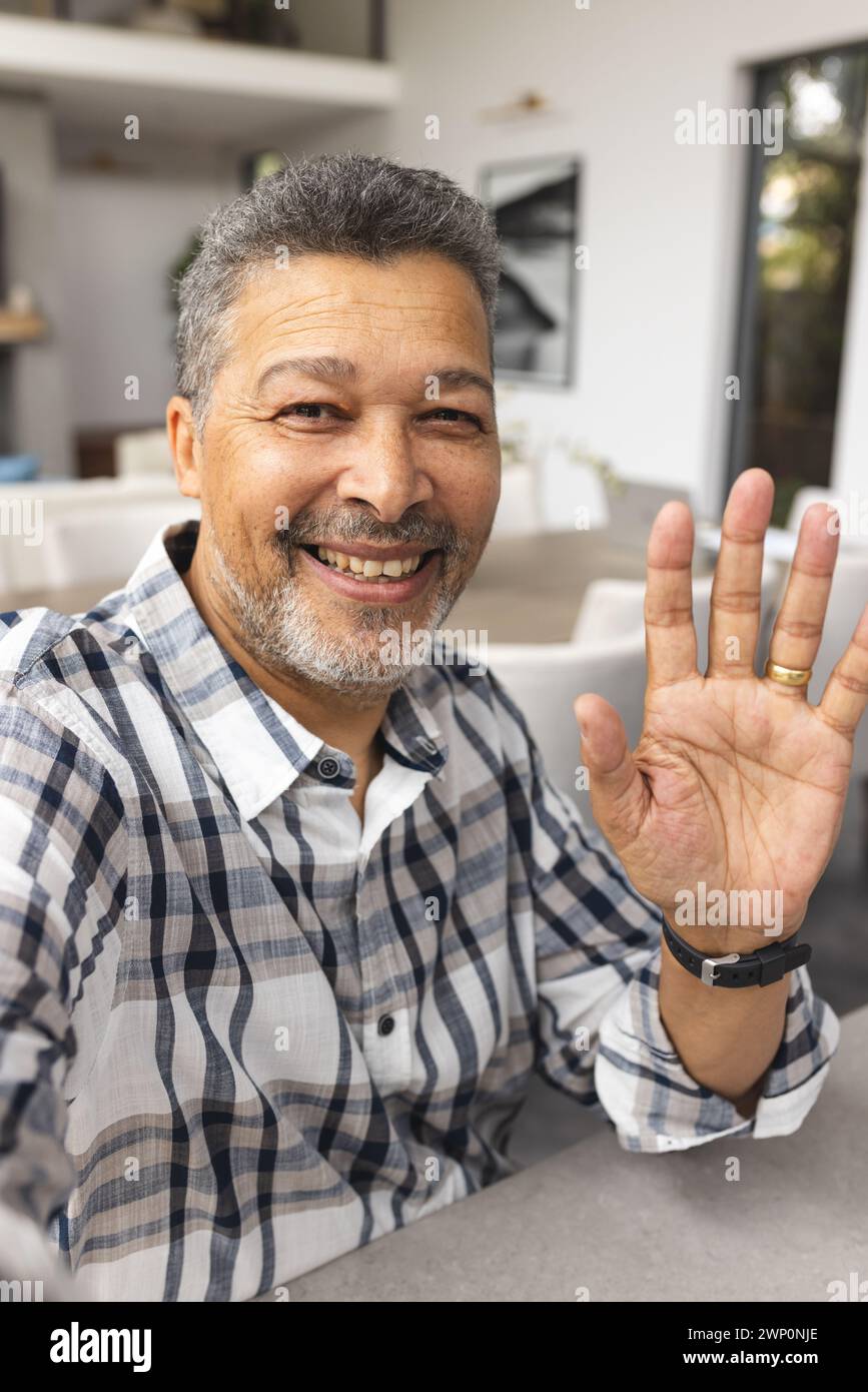 Hombre mayor biracial con ondas de pelo gris en la cámara en una videollamada, luciendo una sonrisa cálida Foto de stock