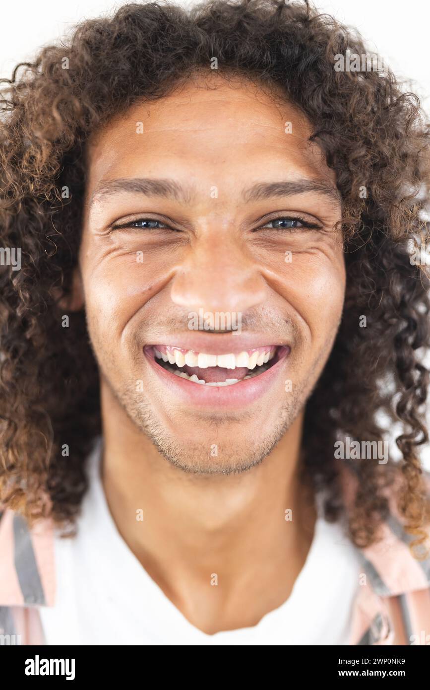 El joven hombre biracial con el pelo rizado sonríe ampliamente, mostrando alegría Foto de stock