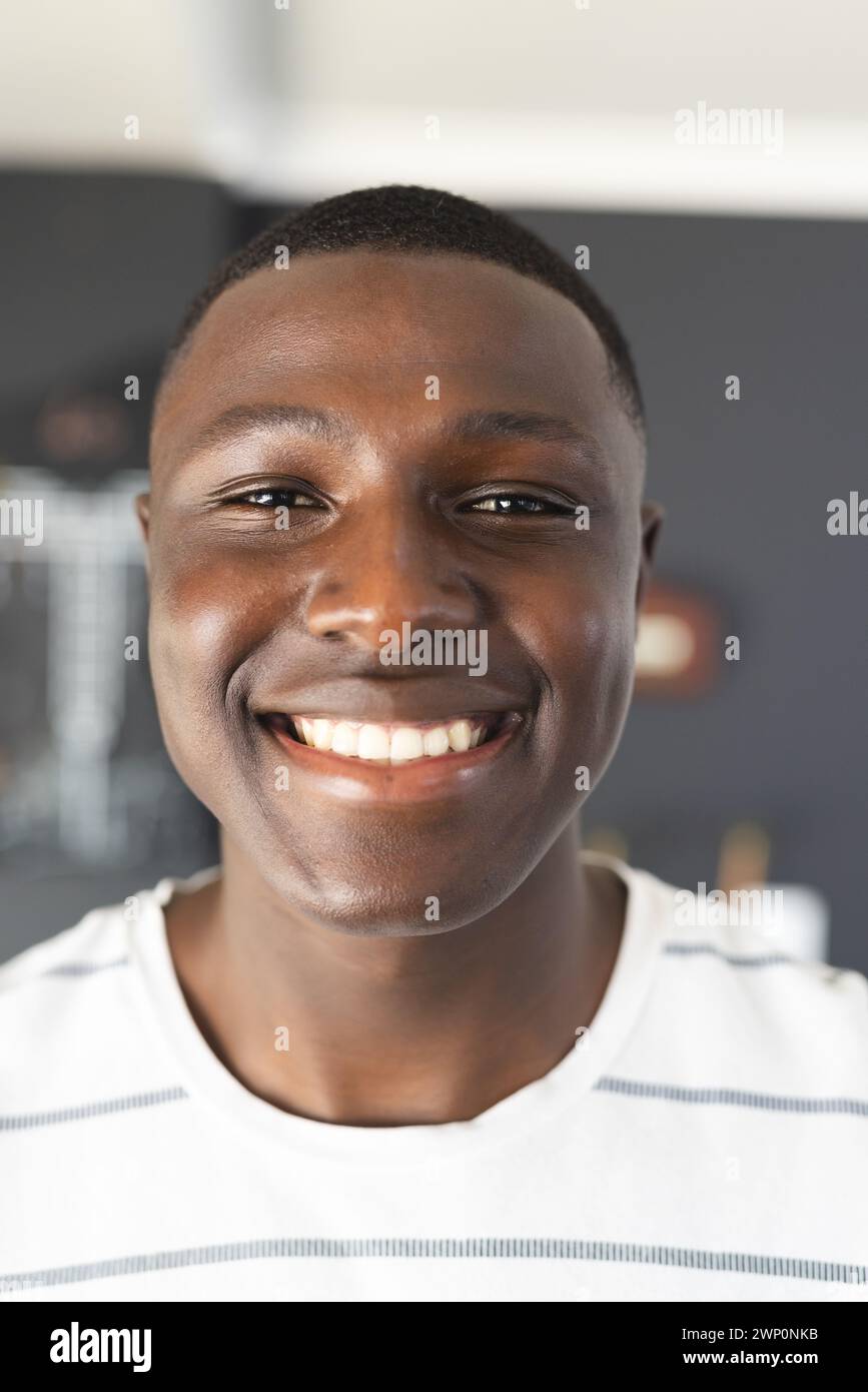 Un joven afroamericano sonríe brillantemente, con una camisa blanca de rayas Foto de stock