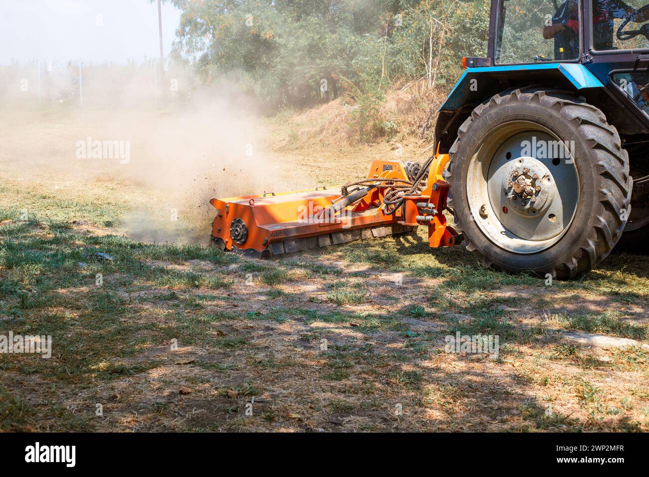 Un tractor con un triturador tritura y nivela la capa superior del suelo. Trabajo agrícola. Foto de stock