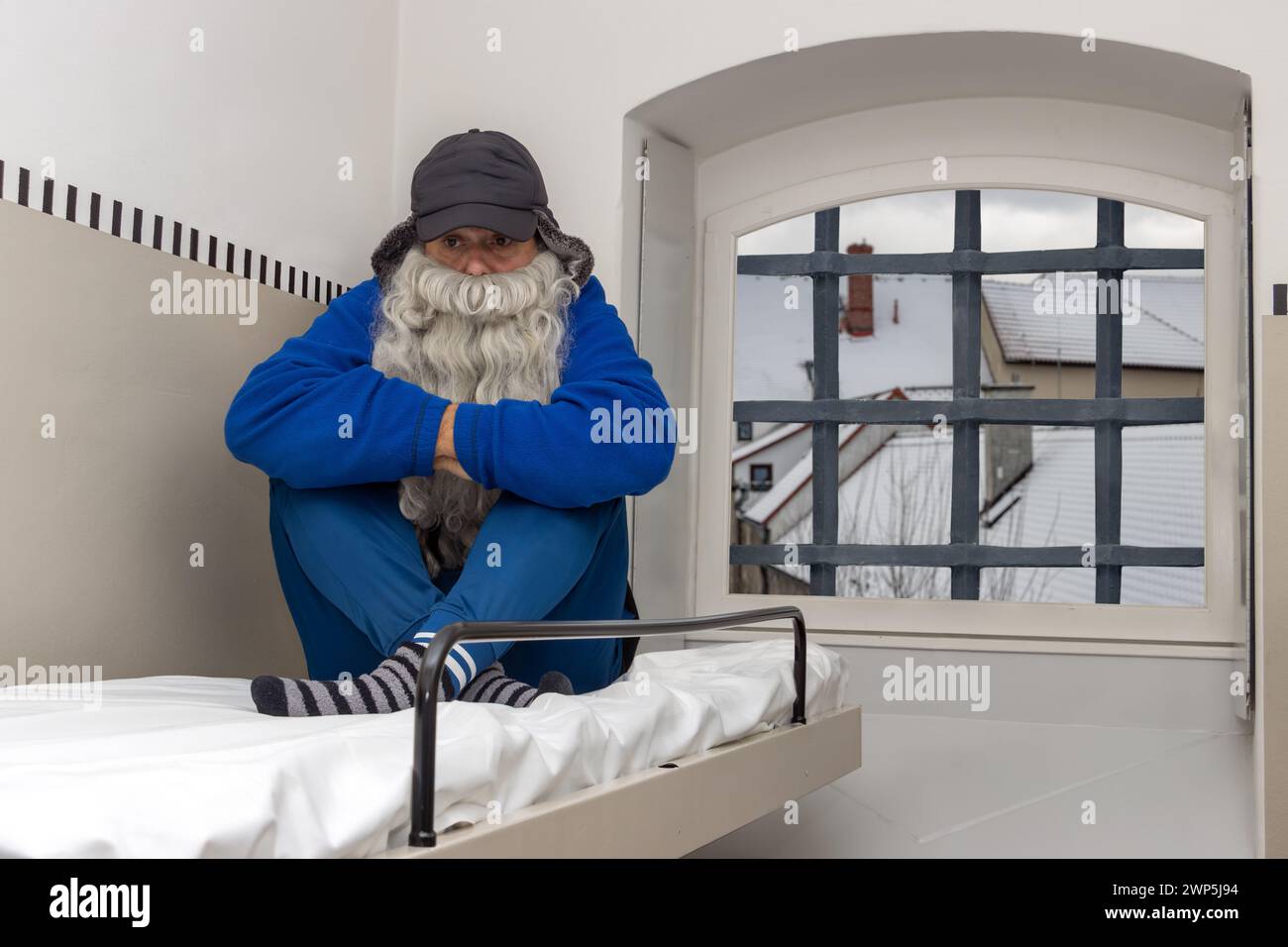 Un hombre barbudo se sienta en una litera en una celda fría de la prisión Foto de stock